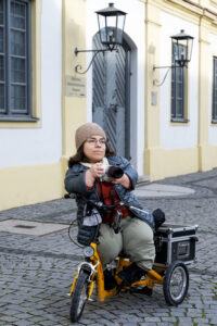 Ableismus im Hochschulwesen - Andrea Schöne auf einem 'Dreirad' mit einer Kamera in der Hand, Foto Kurt Steinhausen